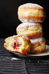 A stack of three sufganiyot donuts with jelly on black background