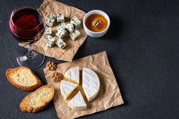 Obraz na płótnie Canvas Camembert cheese, blue cheese, toasts, honey, walnuts and glass of wine on a dark background. Flat Lay.