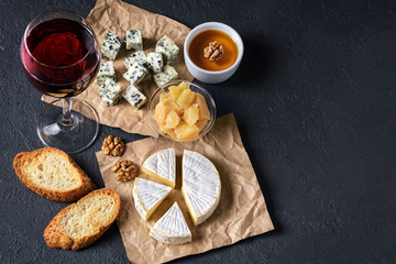 Fototapeta na wymiar Camembert cheese, blue cheese, parmesan, toasts, honey, walnuts and glass of wine on a dark background. Flat Lay.