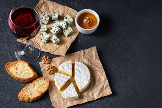 Camembert cheese, blue cheese, toasts, honey, walnuts and glass of wine on a dark background. Flat Lay.