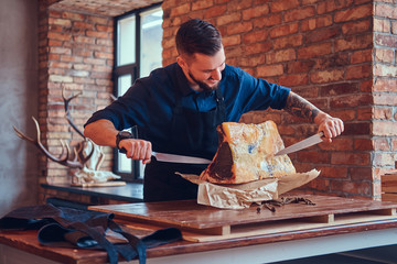 Professional butcher is cutting raw smoked meat on a table for c