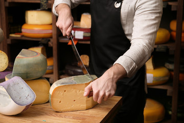 Young worker cutting cheese in shop