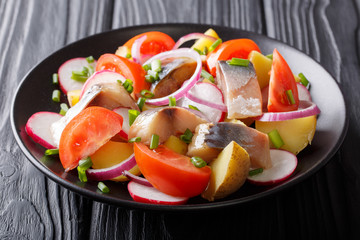 Fish salad: smoked mackerel with potatoes, radish, onions and tomatoes close-up on a plate on a table. horizontal