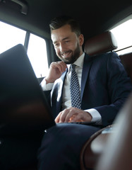 Caucasian male business executive travelling by a car and working on laptop computer.