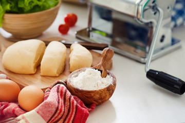 Fresh dough for pasta and pasta machine on kitchen table with ingredients