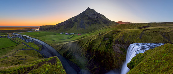 A panorama of Iceland's Skogafoss waterfall, the valley below, and the Skoga River as the sun sets behind the mountain  © Janelle