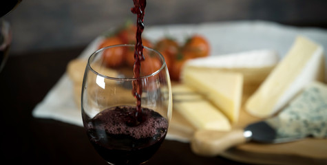 Obraz na płótnie Canvas Red wine poured into a glass with cheese board 
