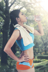 Beautiful slim woman with resting after jogging while drinking water at city park