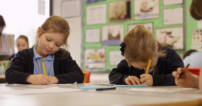 4k, Two cute little girls sitting in class with her teacher and classmates blurred in the background. Slow motion.