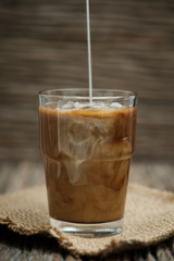Classic still life with The hand is pouring milk to a glass of coffee, vertical vintage picture.