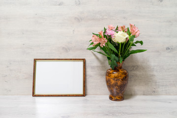 Colorful spring bouquet of rose, chrysanthemum and alstroemeria flowers in a vase with empty photoframe on wooden background