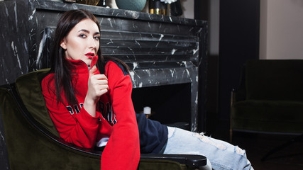Trendy young woman ia a red hoodies. Portrait in fashionable interior.