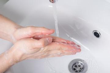 Fototapeta premium Washing hands with soap under running water, on a light background of a shell