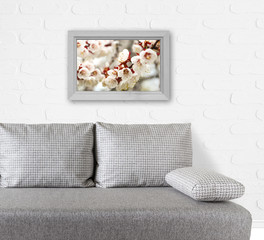 Wooden frame with floral poster over modern couch near white bricks wall