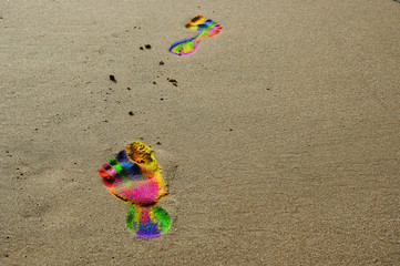 Ślady stóp w kolorach tęczy na plaży.