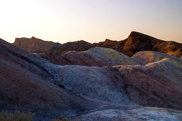 Fototapeta premium Setting Sun on the colorful eroded mountains ridges, ancient rock formations of the hottest place on earth, Death Valley National Park, Zabriskie Point peak, road trip the Amargosa Range, California