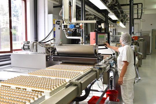 Arbeiterin an einer Produktionslinie f&uuml;r S&uuml;ssigkeiten bedient eine Maschine in der Lebensmittelindustrie // Worker on a production line for sweets operates a machine in the food industry