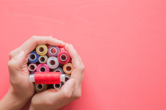 Colorful spools of threads in hands on the pastel pink background. Mock up for dressmakers or textile shops offers as advertising or other ideas. Womanly hobby. Sewing concept. Empty place for text.
