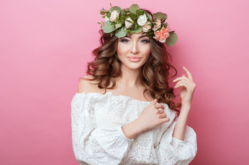 Portrait of beautiful young sexual sensual woman with perfect skin make up curly hair and flowers on head on pink background. Wreath of flowers Spring Summer Fashion Lifestyle People concepts.