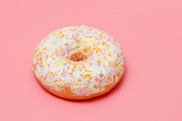 donut with white icing on a pink background. One donut sprinkled with candy.