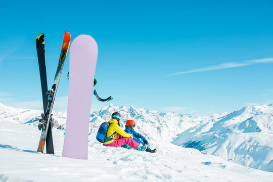 Photo of snowboard, skis on background of sitting sports couple on snowy hill