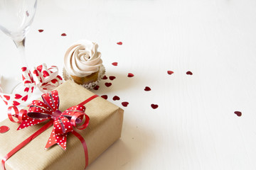 Gift box with red bow, glass and cup cake on white wooden background. Present for woman's day or valentines day. 