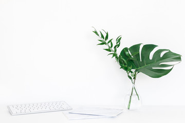 Desk with computer, notebook, green leaves. Creative workspace. Front view, copy space