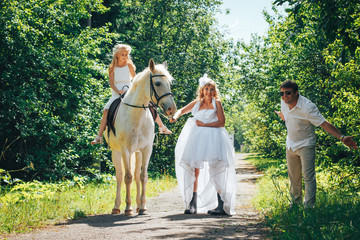 Man, woman dressed as a bride, girl and white horse in the park