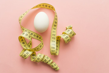 White egg with tailor's meter on pink pastel background. minimal concept. top view
