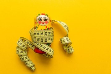 nesting doll or matrioshka with tailor's meter on orange or yellow background. minimal concept. top...