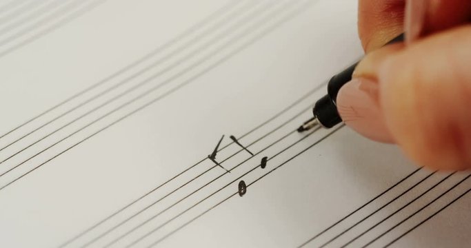 Macro of the female hand writing notes in the musical notebook. Close up