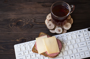 Cup of tea, keyboard with sandwich on the table
