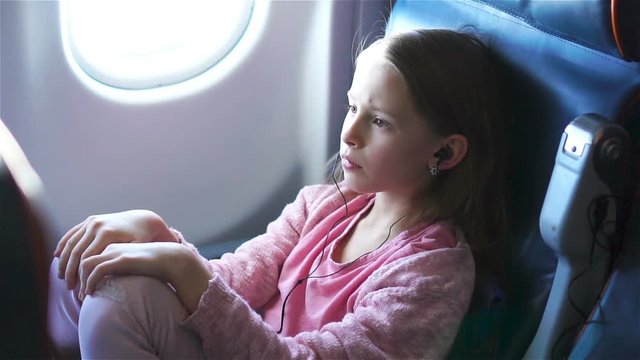 Adorable little girl traveling by an airplane. Cute kid sitting near window in aircraft