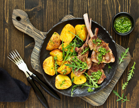 Chops of lamb on bone, with baked potatoes and pesto sauce.