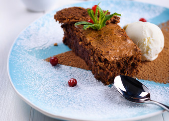Tasty chocolate cake with ice cream, mint and berries on plate on the table on light background, close-up. Chocolate brownie