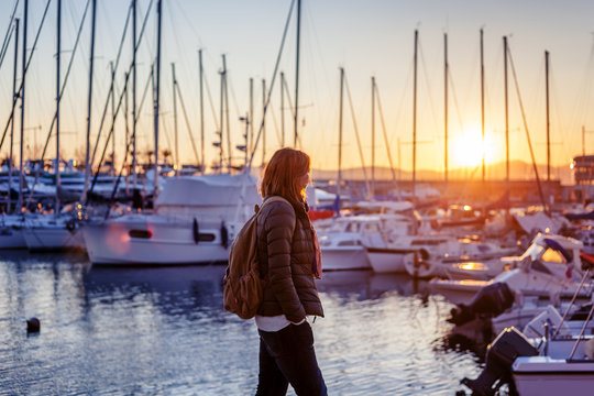 young woman walking in the port by the sea at sunset, traveling to europe