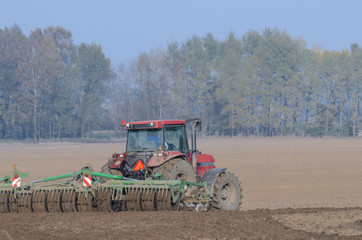 Obraz premium FARM - Tractor while working on a plowed field