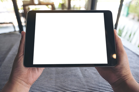Mockup image of hands holding black tablet pc with blank white desktop screen on table with blur background in cafe