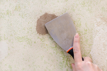 female hand with a paint spatula and putty on the wall
