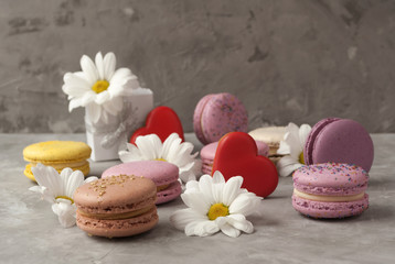 Fototapeta na wymiar Flowers, colorful macarons, heart shaped cookies, gift box on grey background. Close-up.