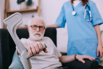Obraz premium Nurse standing behind senior man with crutch