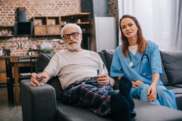 Obraz premium Senior patient with pills and nurse sitting on sofa