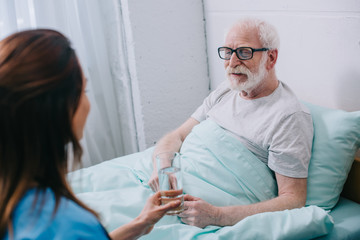 Nurse giving old man in bed a glass of water - obrazy, fototapety, plakaty