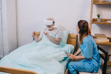 Nurse sitting by old man using vr glasses