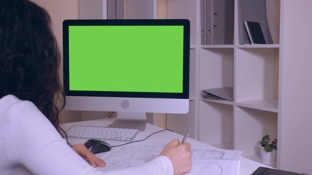back view architect working with blueprint. unrecognisable engineer or designer sitting at the working place with paper documents and green screen computer