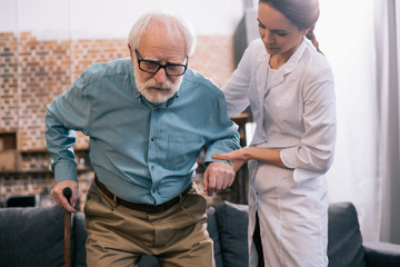 Old man leaning on cane and female doctor hand