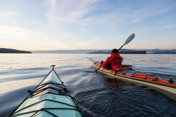 Man on Sea Kayak is kayaking during a vibrant winter sunset. Taken near Jericho Beach, Vancouver, BC, Canada.