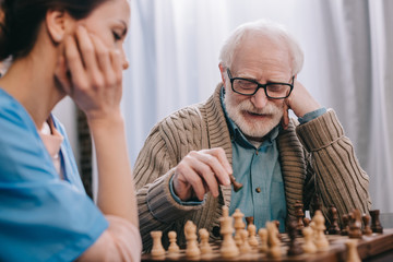 Senior man enjoying playing chess with nurse - obrazy, fototapety, plakaty