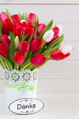 Fresh red tulip flowers bouquet on shelf in front of wooden wall.