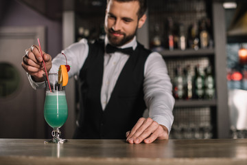 smiling bartender adding plastic straw to cocktail